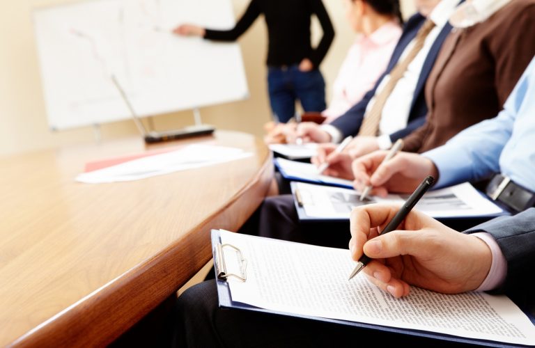 Close-up of businesspeople hands holding pens and papers near table at business seminar